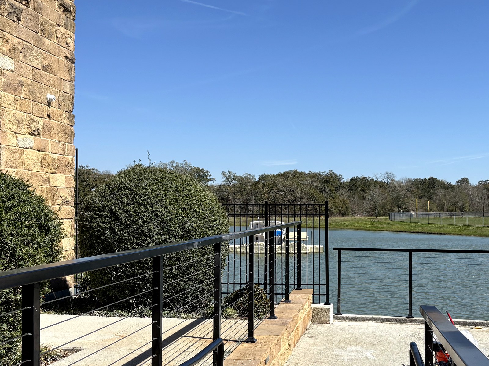 Black metal cable railing and ornamental iron fence along a lakefront walkway in the Meridiana community in Manvel, TX