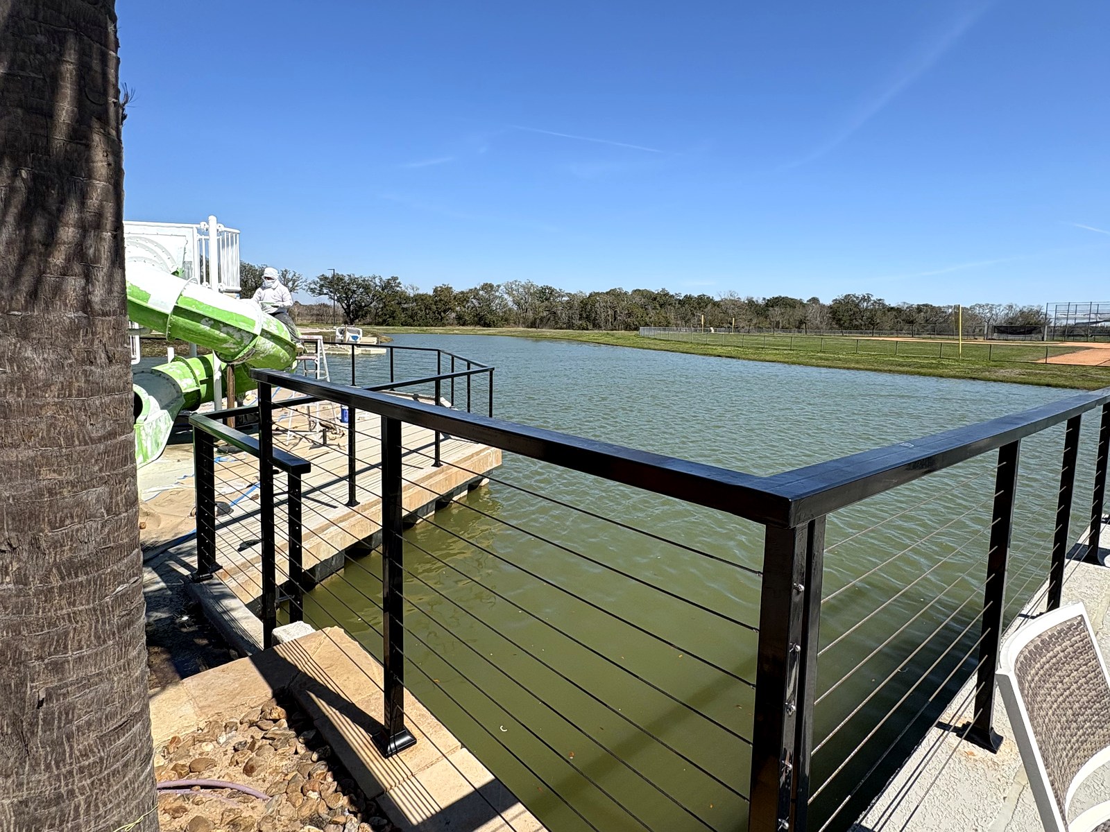 Custom black steel cable railing installed around a lakeside pool deck in Meridiana, Manvel, TX
