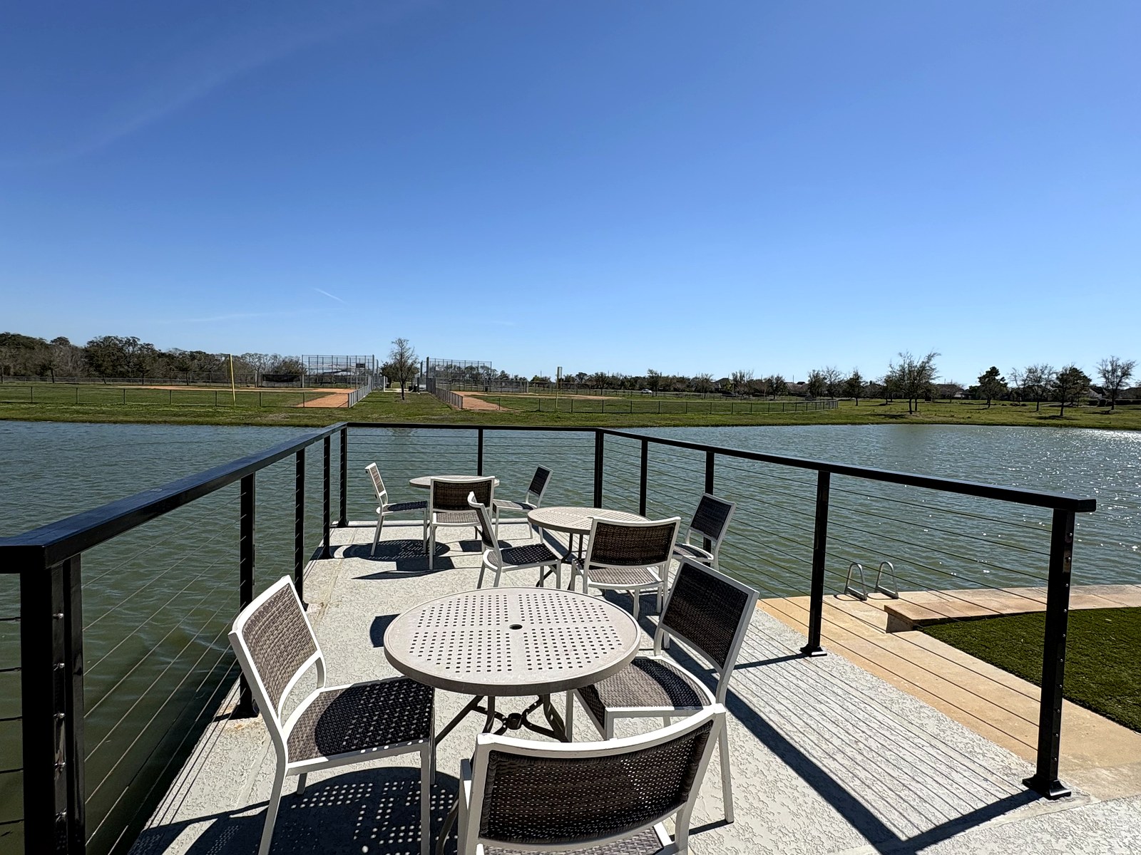 Black cable railing enclosing a lakefront dining terrace at a community amenity center in Meridiana, Manvel, TX