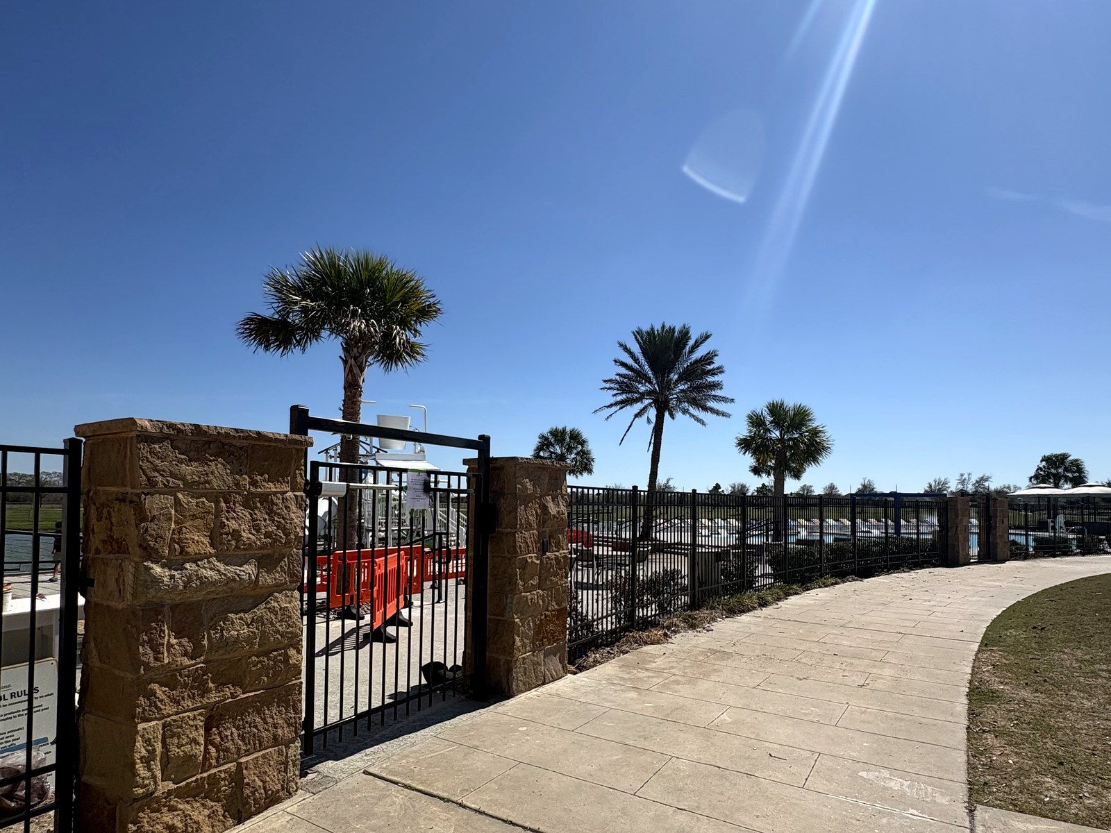 Black ornamental iron pool fence and self-closing access gate with stone columns at a community amenity center in Meridiana, Manvel, TX